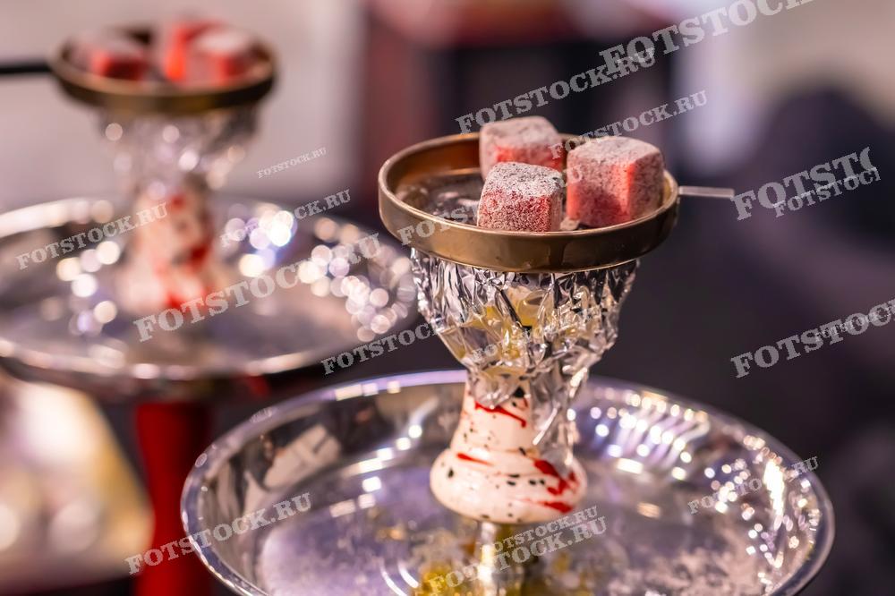 Фотография изображает кальяны с раскаленными углями, готовыми к использованию. Угли размещены на металлических чашах кальянов, создавая атмосферу расслабленного отдыха и наслаждения кальяном в кальянной.